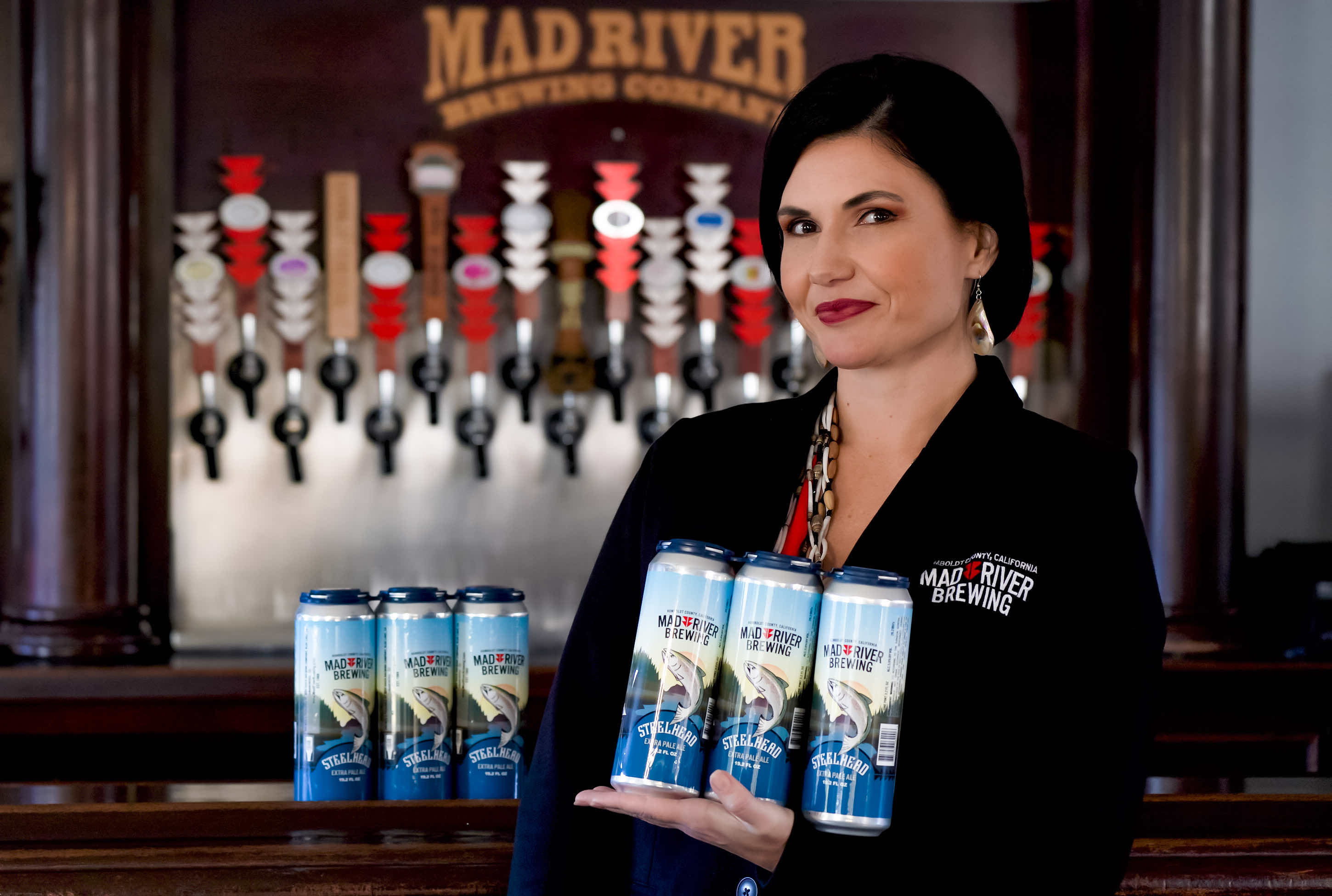 Linda Cooley, Chief Operating Officer and Yurok citizen, holding a 3-pack of Steelhead Extra Pale Ale in 19.2 oz cans. (image courtesy of Mad River Brewing)